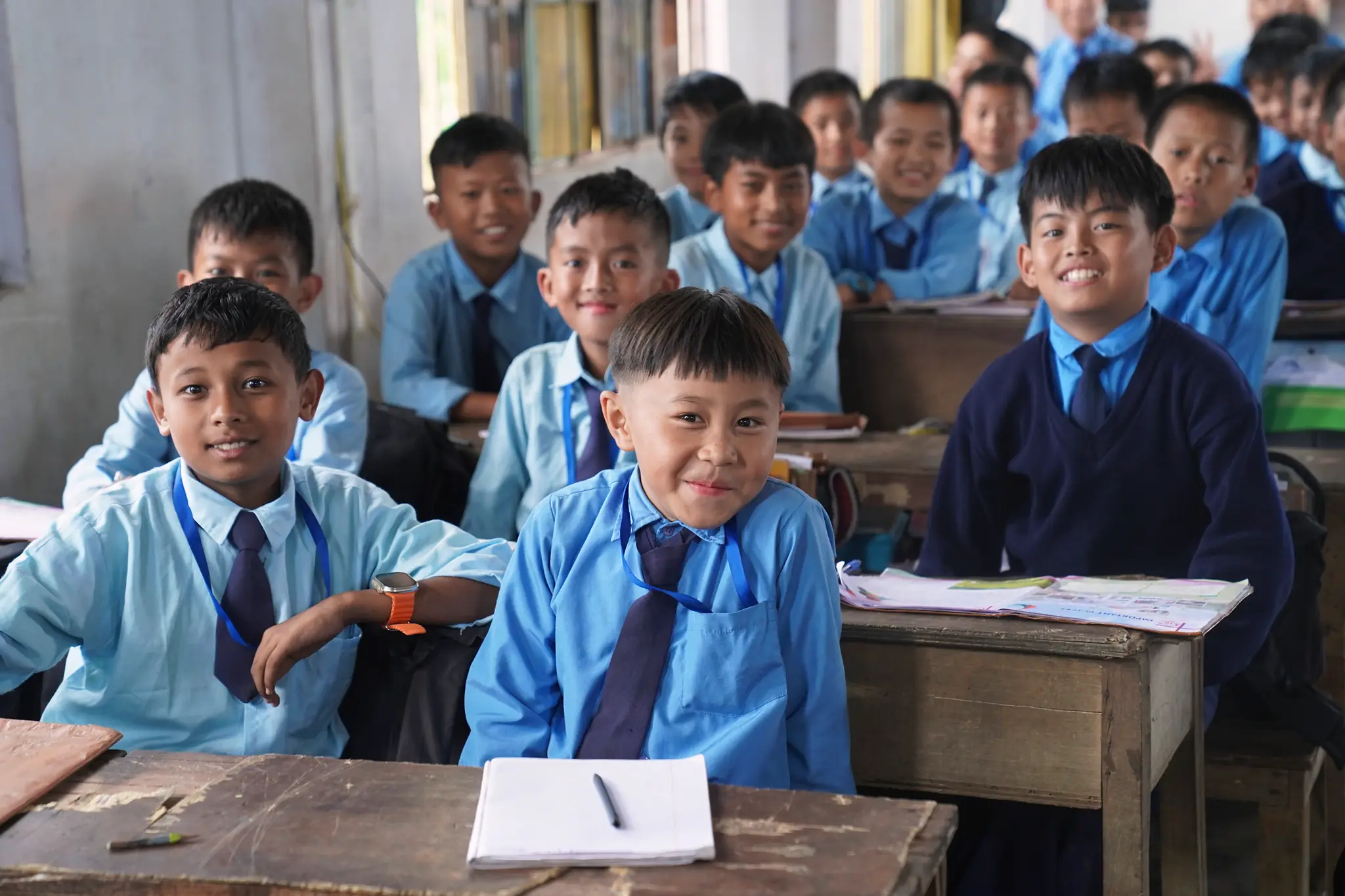 Smiling students in school uniform at their desks in a classroom